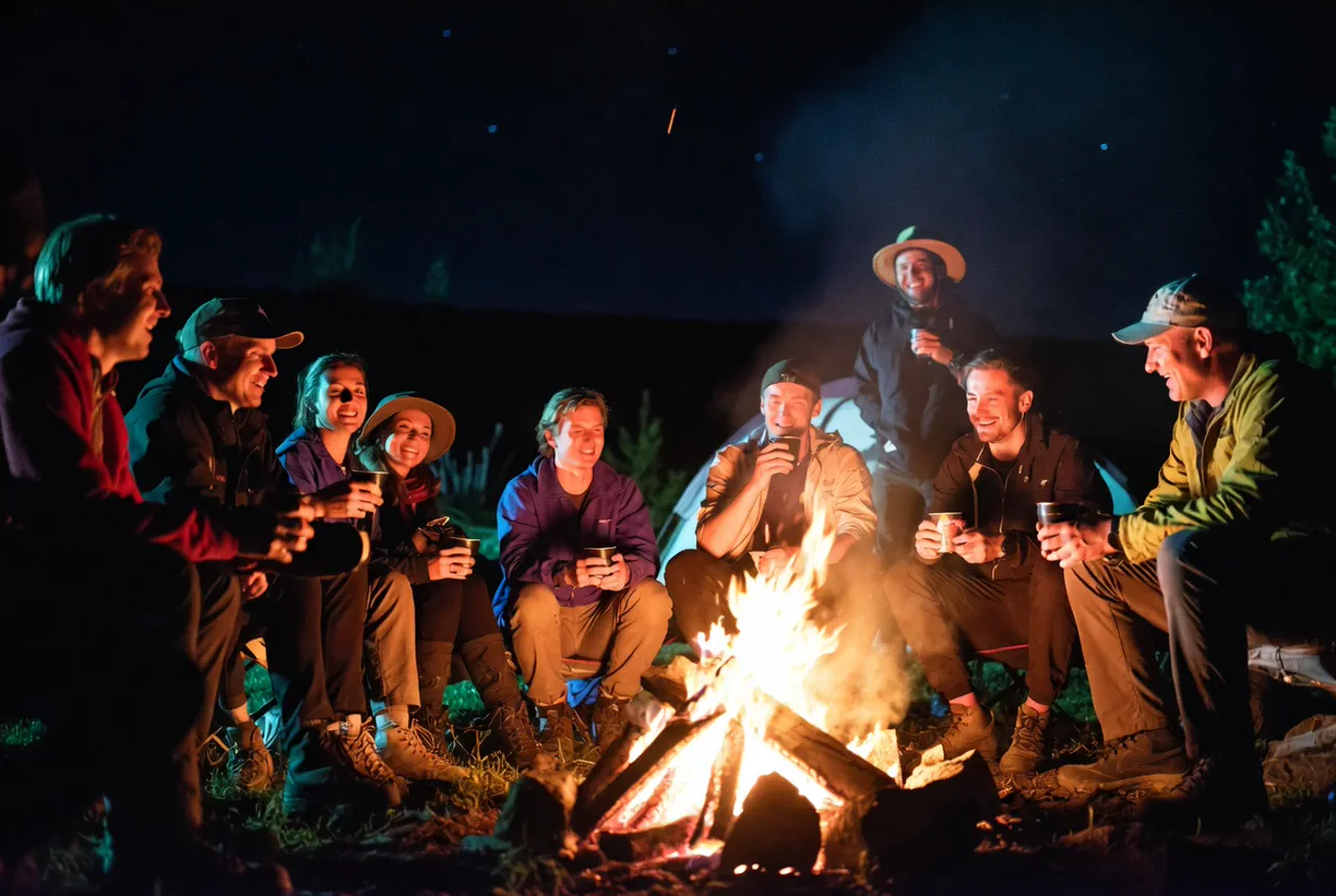 Glückliche Gruppe sitzt abends am Lagerfeuer und erzählt Geschichten